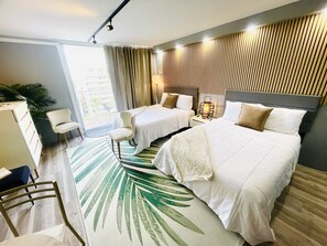 Ein Hotelzimmer mit zwei Betten, einem Schreibtisch, einem Stuhl, einem großen Fenster und Blick ins Freie.