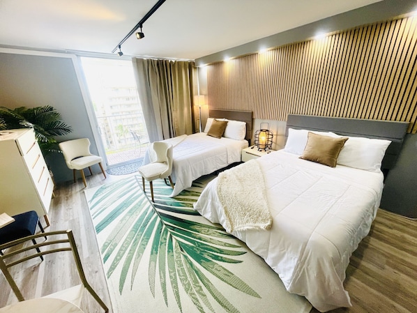 A hotel room with two beds, a desk, a chair, a large window, and a view of the outside.