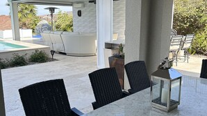 Ein überdachter Patio-Bereich mit einem Marmortisch, schwarzen Korbstühlen, einem weißen Outdoor-Sofa und einer Laterne.