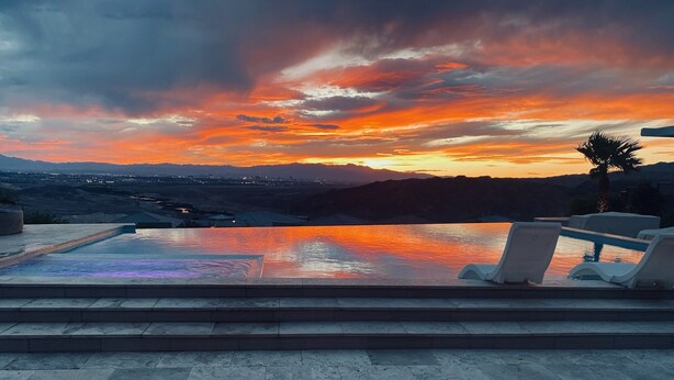 Ein Infinity-Pool mit Blick auf einen Sonnenuntergang über Bergen.
