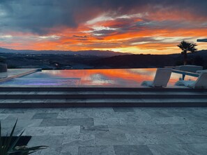 Una piscina infinita con vista a la puesta de sol sobre montañas.