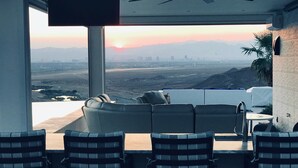 Ein modernes Wohnzimmer mit großem Fenster, das Blick auf eine Stadtlandschaft und Berge bietet. Es gibt vier gestreifte Sessel und ein Sofa.