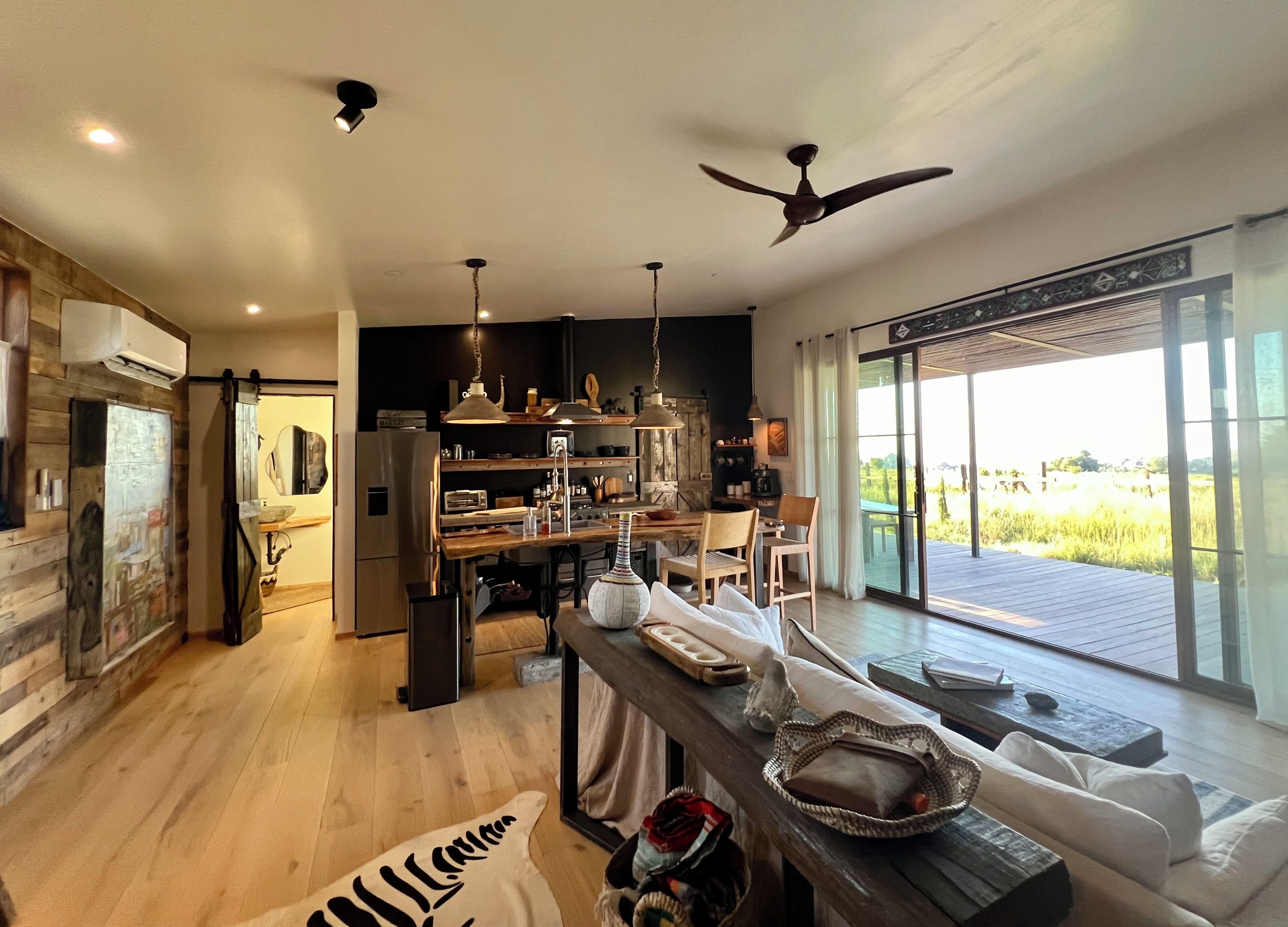 Una cocina moderna con armarios de madera, una isla central, iluminación colgante y un gran ventanal corredero que da a una terraza.