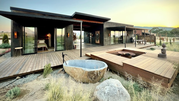 Un espacio habitable exterior moderno y de varios niveles con una gran cuenca de piedra, terrazas de madera y paredes de cristal que ofrecen vistas amplias.