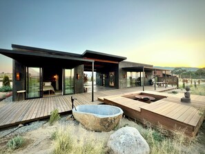 Un espace de vie extérieur moderne, aménagé sur plusieurs niveaux, avec un grand bassin en pierre, des terrasses en bois et des murs de verre offrant une vue panoramique.