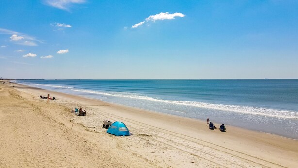 A beach with a tent, a beach chair, and a few people. - Tranquil Breeze-5 min. walk to the beach! Book now for great fall/winter rates! (Oak Island)