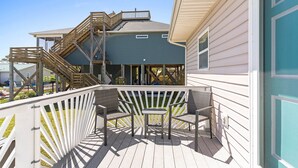 A wooden deck with a white railing, a small table, and two chairs. - Tranquil Breeze-5 min. walk to the beach! Book now for great fall/winter rates! (Oak Island)