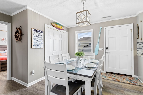 A dining area with a white table set for four, a potted plant, and a wall-mounted sign reading "BEACH RULES".