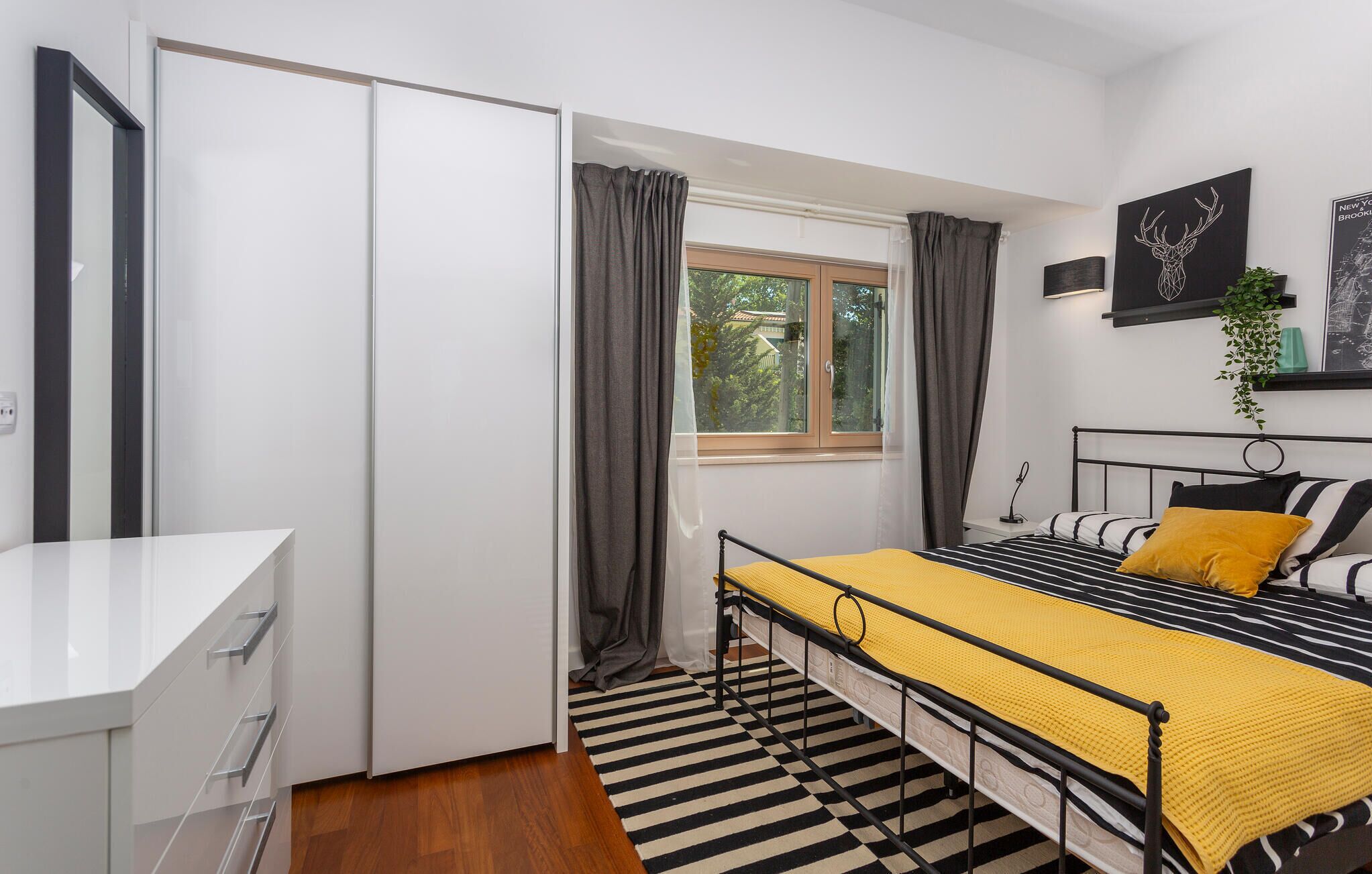 Un dormitorio moderno con cama, mesita de noche y ventana con cortinas.