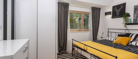 Un dormitorio moderno con cama, mesita de noche y ventana con cortinas.
