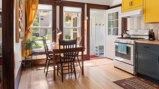A kitchen with wooden flooring, a dining table with chairs, a stove, and yellow cabinets. - Cozy and charming. Your home away from home in the heart of Viroqua. (Viroqua)