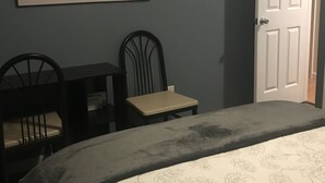 A bedroom with a bed, a desk, two chairs, a door, and a painting of a pier on the wall. - Quiet, 3 bedroom & 1 bath get-a-way. Near Lake Erie for fishing & skiing resorts (Albion)