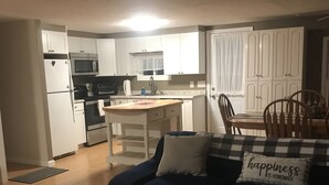A living room with a dark blue sofa, a coffee table, and a kitchen area in the background. - Quiet, 3 bedroom & 1 bath get-a-way. Near Lake Erie for fishing & skiing resorts (Albion)