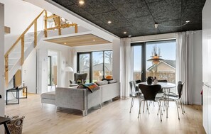 A spacious living area with a grey sofa, a dining table with chairs, a staircase, and large windows offering a view of the outside. - Awesome home in Haderslev with WiFi (Haderslev)