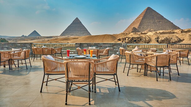 Un espace extérieur aménagé avec des chaises et des tables en osier, offrant une vue sur les pyramides.