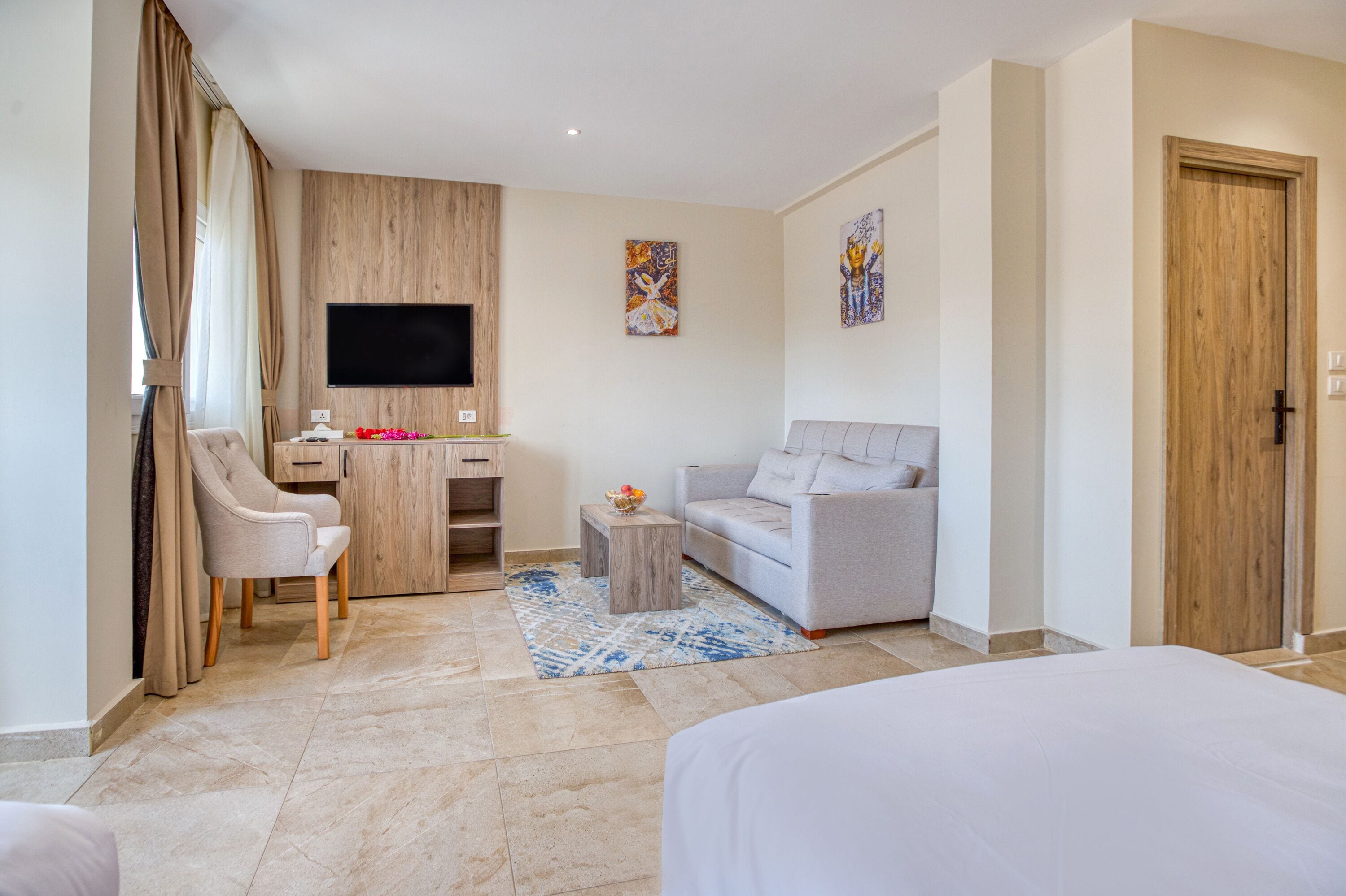 Een moderne hotelkamer met een bed, een slaapbank, een bureau met een flatscreen-televisie en een houten garderobe.