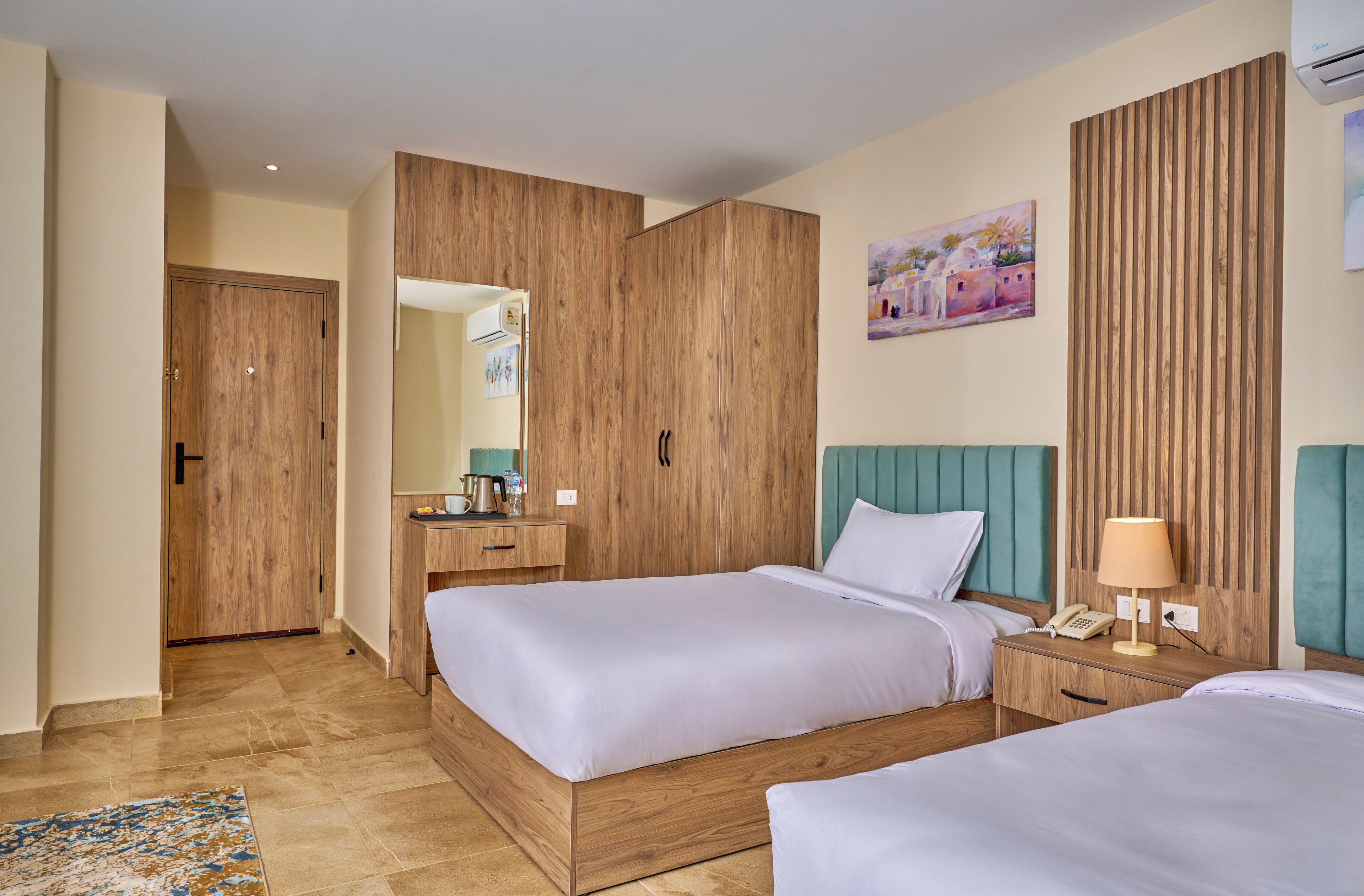 Hotelkamer met twee bedden, houten hoofdeinden, een nachtkastje met lamp en een schilderij aan de muur, plus een houten garderobe.