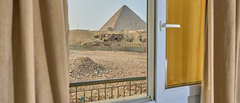 A view of the Great Pyramid of Giza through a window with curtains.