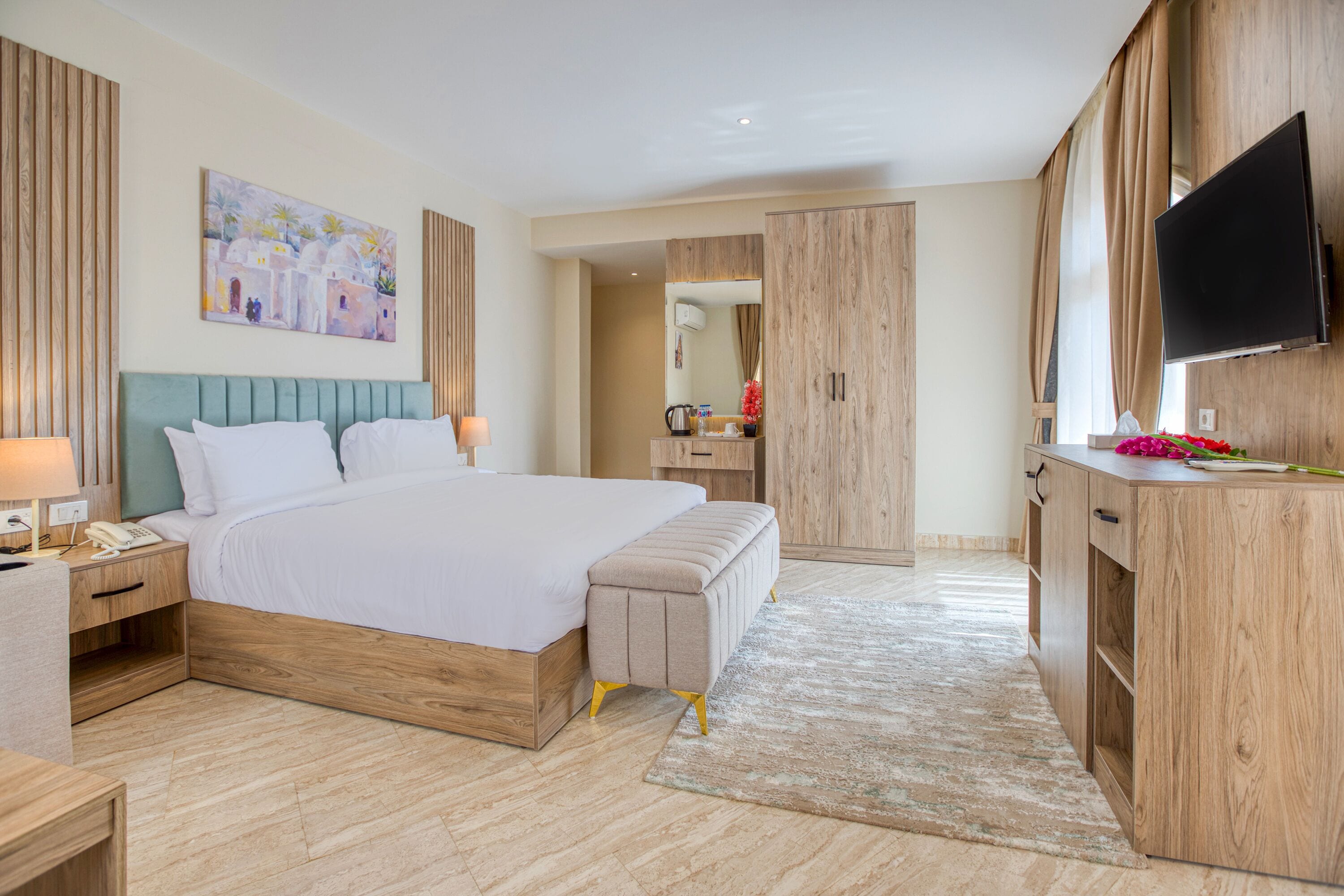 A modern hotel room with a large bed, wooden wardrobe, a flat-screen TV, and a painting on the wall.