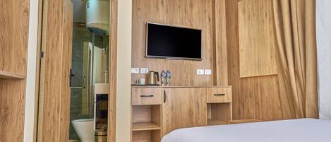 A bedroom with a wooden wardrobe, a TV mounted on the wall, and a shower area visible through an open door.