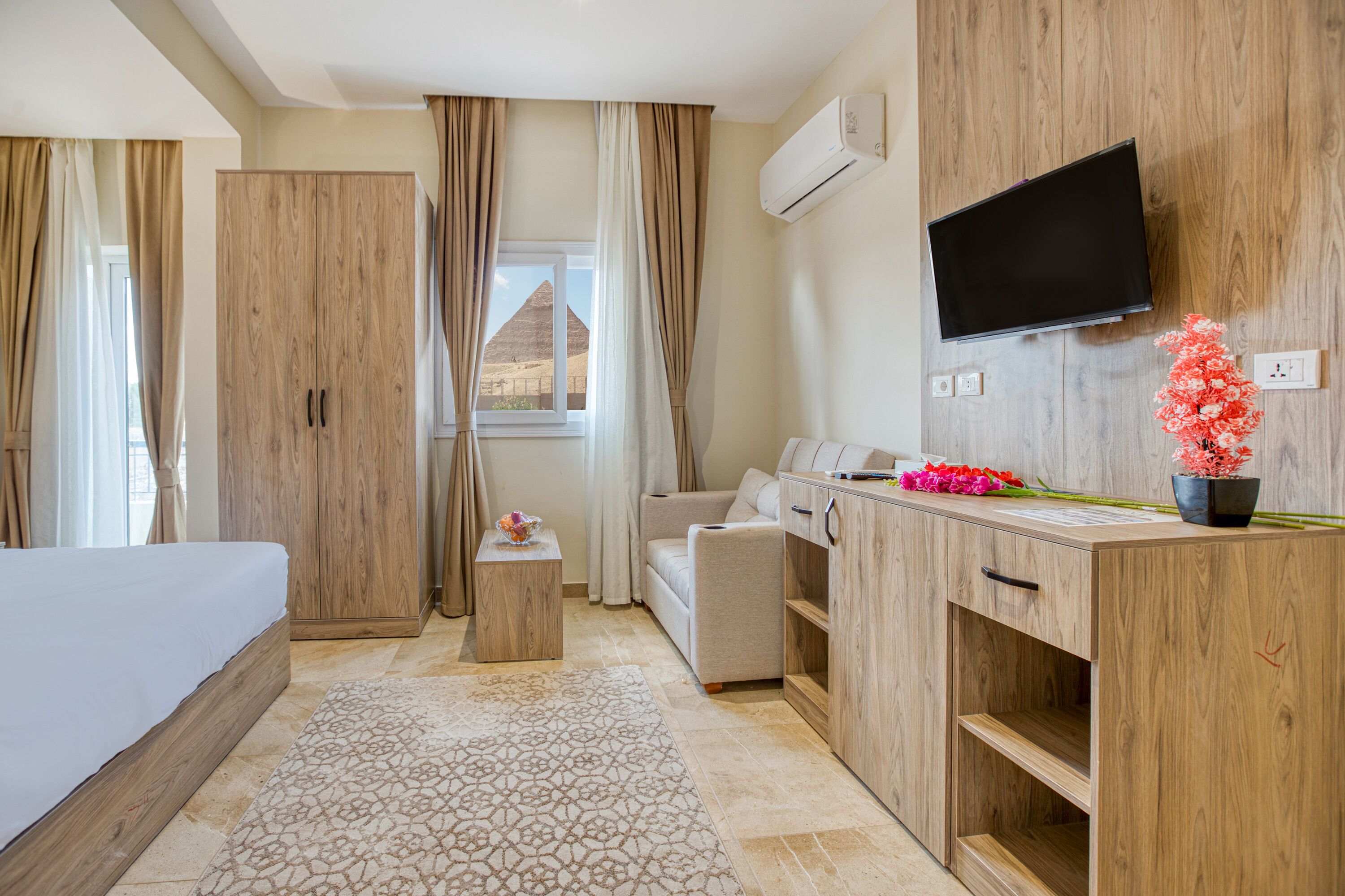 Habitación de hotel con cama, sofá, escritorio con televisión de pantalla plana y ventana con cortinas.