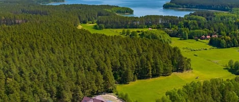 Vista aérea de una zona boscosa con un edificio que cuenta con varias construcciones de techo rojo, rodeado de campos verdes y un lago al fondo.