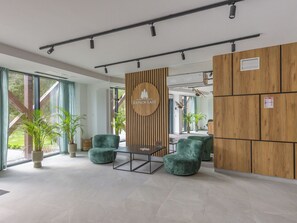 Un espace d’accueil moderne avec un mur revêtu de panneaux en bois, un comptoir d’accueil, deux fauteuils verts et des plantes en pot.