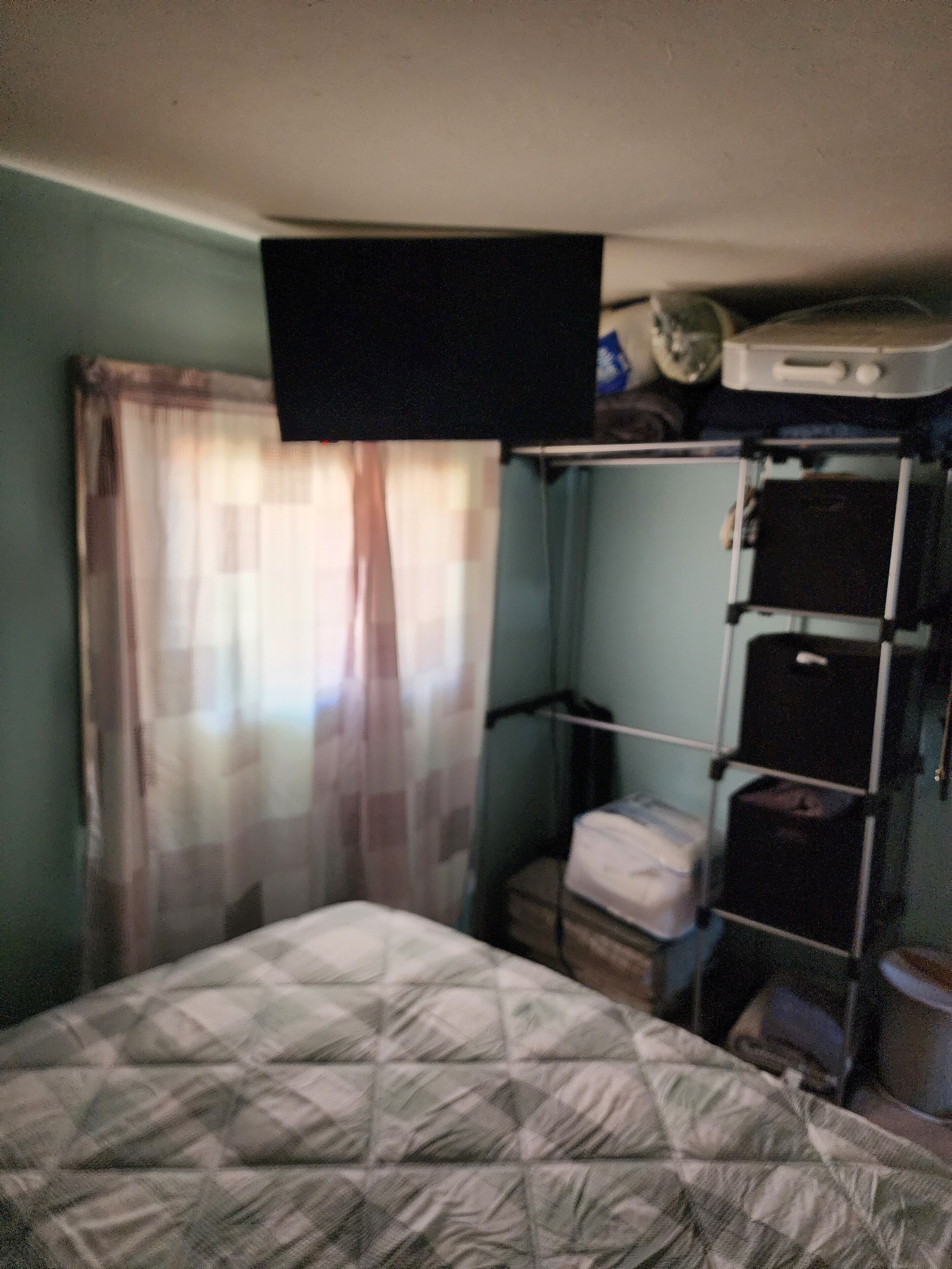 A small, compact room with a bed, a TV mounted on the wall, and a shelf with storage boxes.