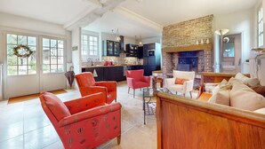 A spacious living room with red and beige sofas, a fireplace, and a kitchen in the background. - Awesome home in St.Marguerite d.Loges with sauna (St.Marguerite d.Loges)