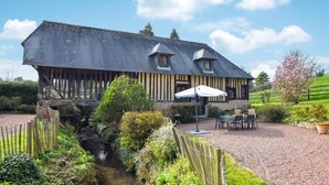 A traditional half-timbered house with a gravel patio, outdoor seating, and a small stream. - Awesome home in St.Marguerite d.Loges with sauna (St.Marguerite d.Loges)