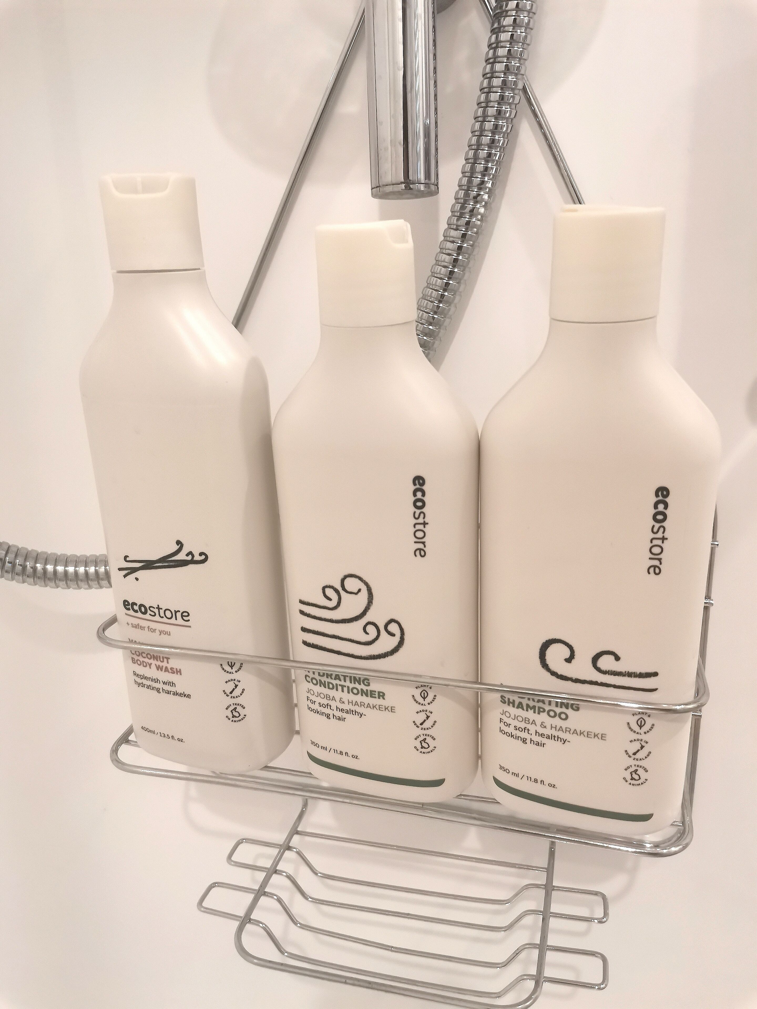 A bathroom with a shower and three bottles of hair care products on a rack.