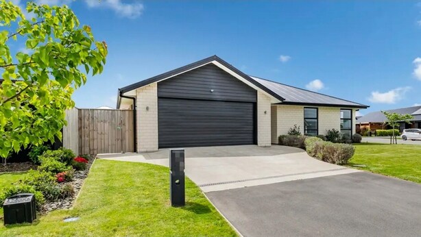 A modern two-story house with a dark garage door, a well-maintained lawn, and a wooden fence.