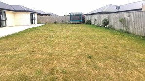 A backyard with a trampoline, a wooden fence, and a house with a garage.