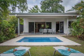 A modern house with a swimming pool, a patio with a table and chairs, and a garden with various plants.