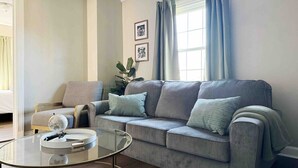 A living room with a grey sofa, a glass coffee table, and a plant. - Spring Street Suites A / Stylish 3BD/1BA Apt (Evansville)