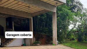 A covered garage with a gravel driveway and a small grassy area. - Studio Flor do Mato (Itapema)
