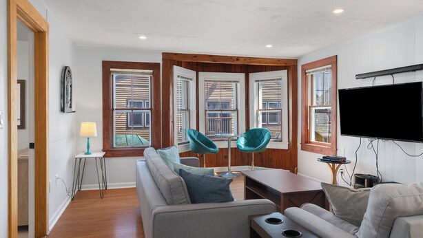 Un salon moderne avec un canapé, deux fauteuils turquoise, une table basse et un téléviseur fixé au mur.