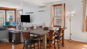 Un salon moderne avec une table à manger en bois, des sièges confortables, un téléviseur à écran plat et un ventilateur de plafond.
