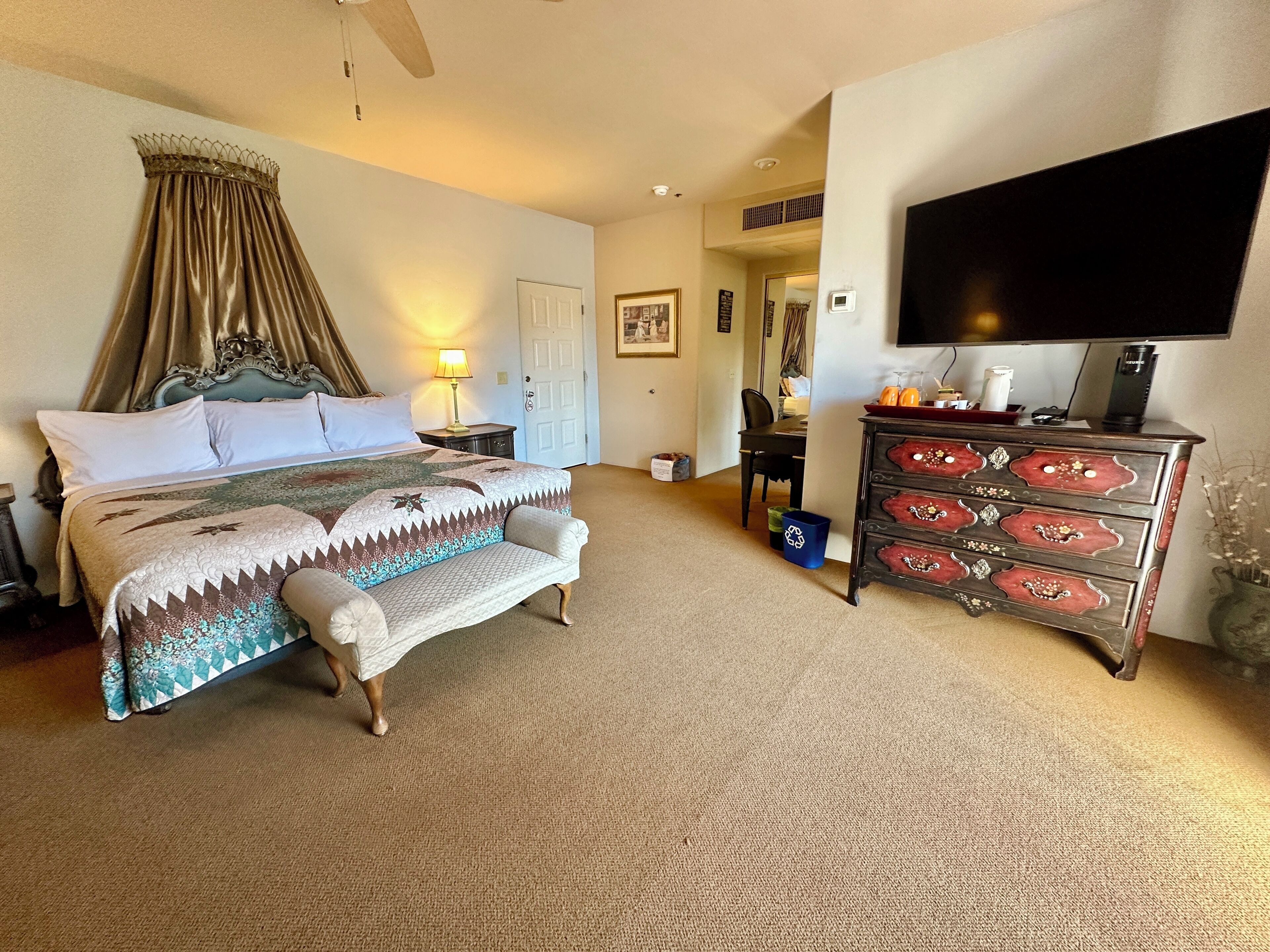 A hotel room with a large bed, a desk, a dresser, and a TV.