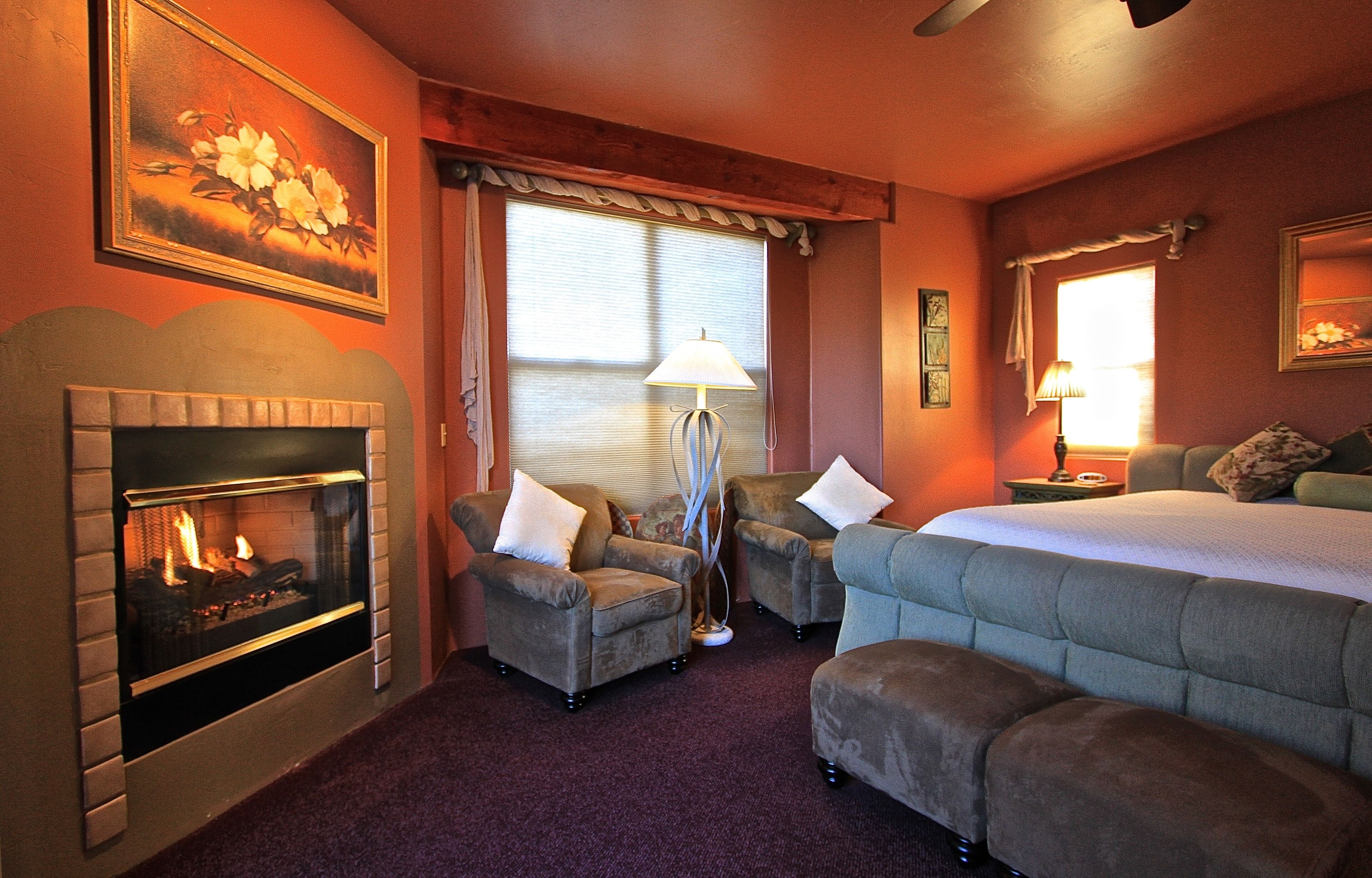 A hotel room with a fireplace, two armchairs, a bed, and a nightstand with a lamp.