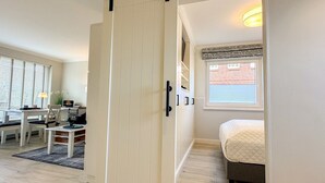 A bedroom with a bed, a desk with a chair, a window with blinds, and a door. - Flow - Haus Alice - Flow (Sylt)