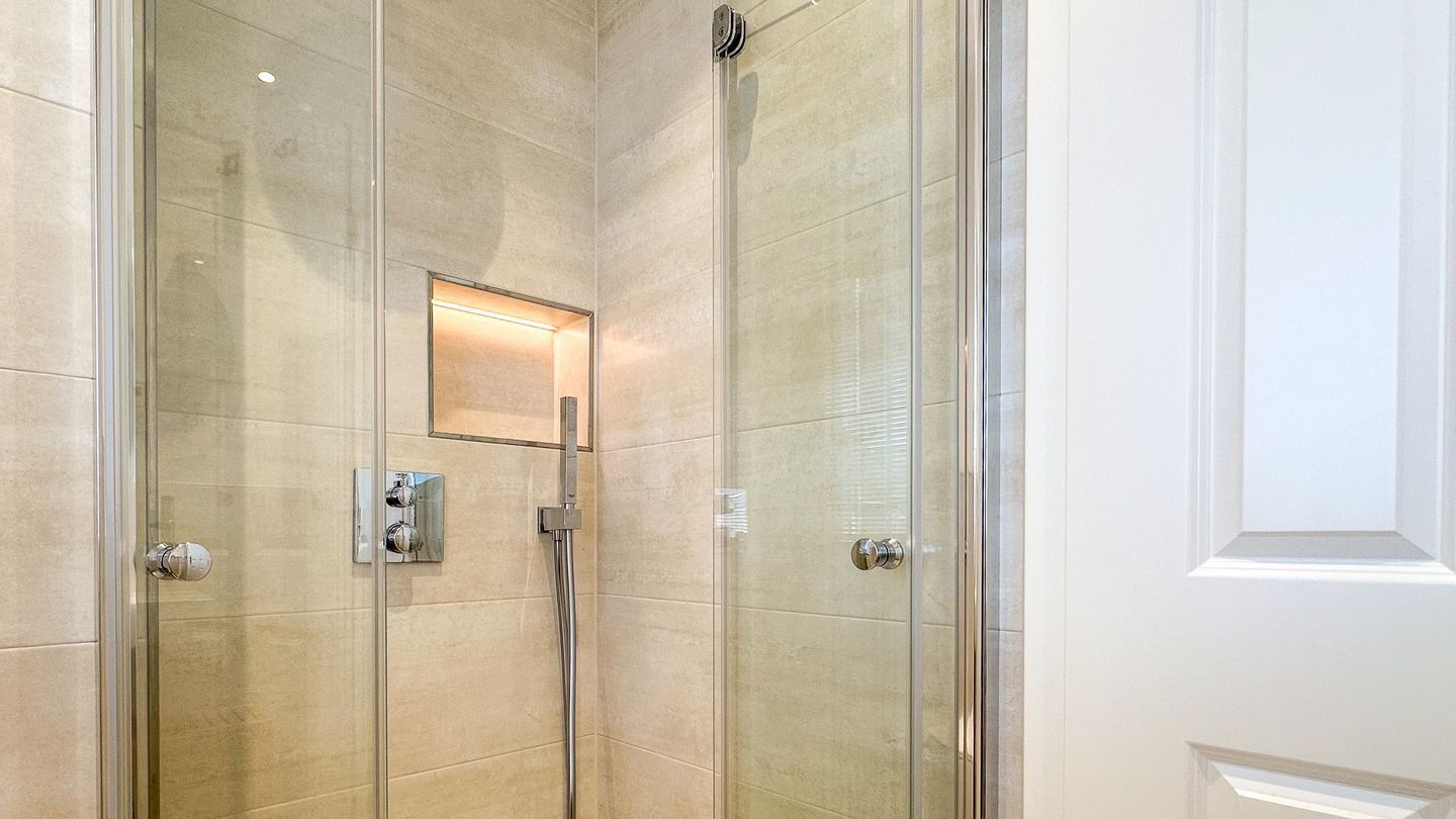A glass-enclosed shower with a control panel, a small mirror, and a light fixture.