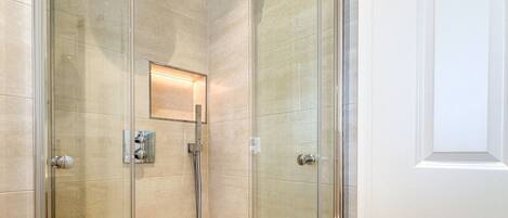 A glass-enclosed shower with a control panel, a small mirror, and a light fixture.