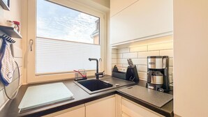 A modern kitchen with a black countertop, a coffee maker, and a window with blinds. - Flow - Haus Alice - Flow (Sylt)