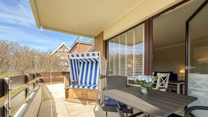 A patio with a striped beach chair, a table with a vase of flowers, and a sliding glass door leading to a room. - Flow - Haus Alice - Flow (Sylt)