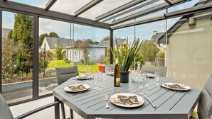A conservatory with a table set for dining, featuring a bottle of wine, glasses, and a potted plant. - Les Jardins du Val by Interhome (Dinard)