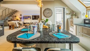 A modern kitchen with a central island, a dining area with a staircase, and a living room with a sofa and coffee table. - Les Jardins du Val by Interhome (Dinard)
