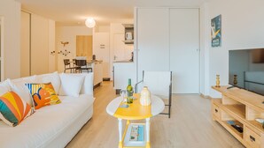 Una sala de estar moderna con un sofá blanco, almohadas coloridas, una mesa de centro amarilla y un televisor sobre un mueble de madera.