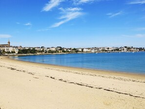 Una playa con cielo azul despejado, orilla arenosa y edificios al fondo.