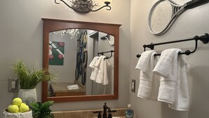 A bathroom with a sink, mirror, towel rack, and tennis racket.